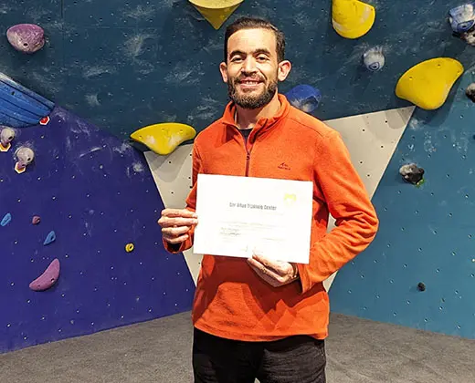 Certified climbing guide in Morocco holding a first aid certificate at an indoor climbing gym
